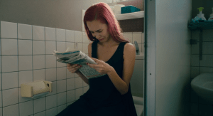 Rei cries in the restroom stall, holding a newspaper. Image: screenshot from "Ride or Die"