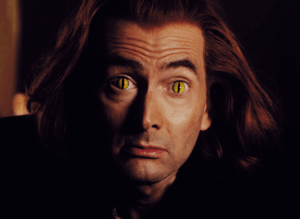 Crowley from Good Omens without his sunglasses, revealing cat-like eyes. His hypnotic stare urges you to take a safe approach to cosplay contacts!