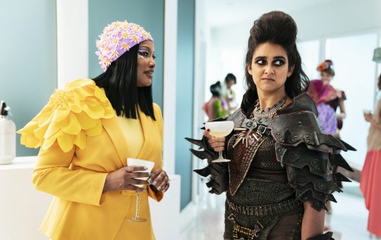 A woman in a Hunger-Games style outfit on the left, talking to a woman in Mad Max gear on the right