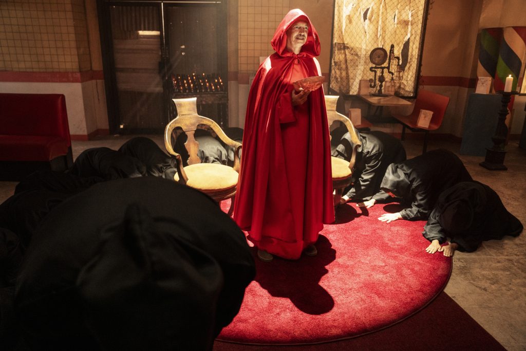 a man in a red cloak stands in the middle of a circle of others