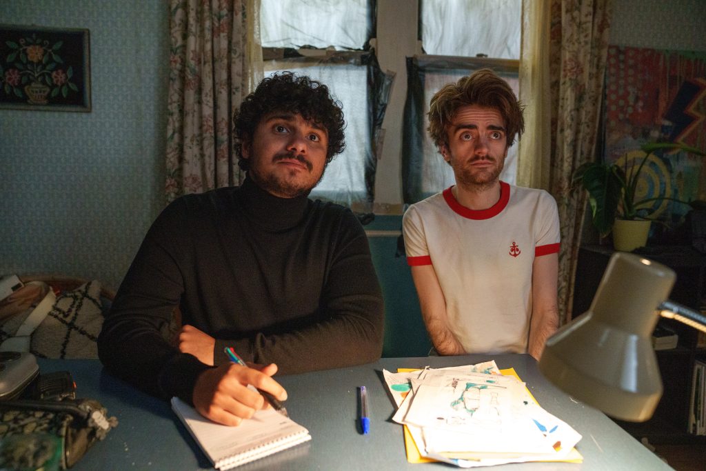 Kash (Bilal Hasna) sets up his vigilante group with Jizzlord the Human (Luke Rollason) looking on.