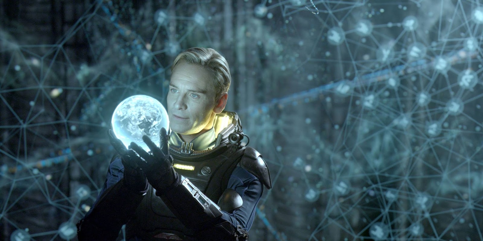 David, a blond man played by Michael Fassbender, standing in the middle of glowing markings floating in the air holding a glowing orb.