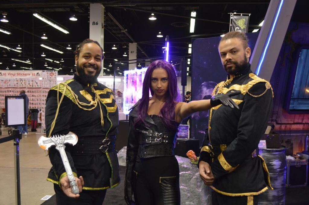 three people (two men and one woman, with the woman in the center) wearing space fantasy type outfits and posing