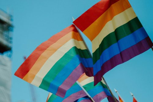 Two rainbow flags stand out against the background of a bright blue sky.