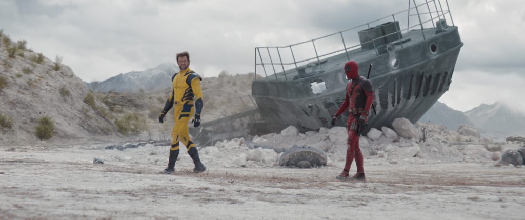 Hugh Jackman as Wolverine (in the yellow suit) and Ryan Reynolds as Deadpool walk across a deserted landscape