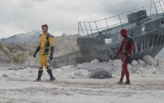 Hugh Jackman as Wolverine (in the yellow suit) and Ryan Reynolds as Deadpool walk across a deserted landscape