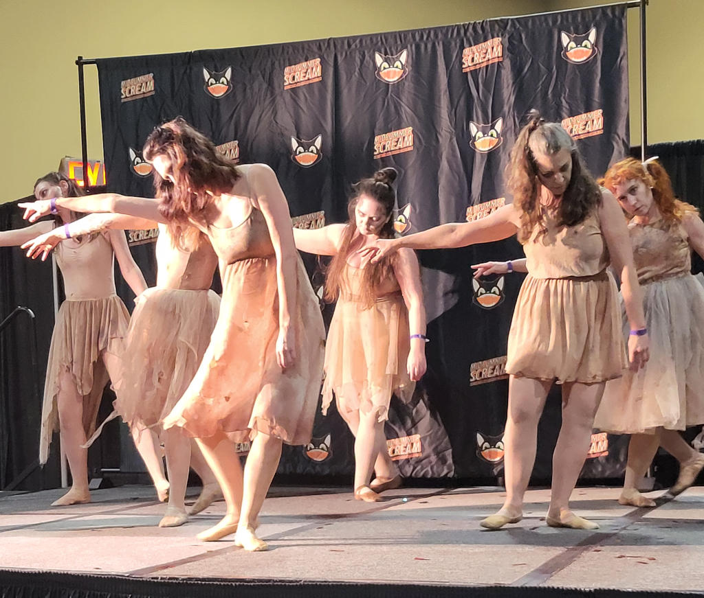 a group of dancers, dressed in bloody shabby clothes, reach to the left, heads down