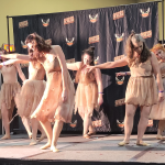 a group of dancers, dressed in bloody shabby clothes, reach to the left, heads down