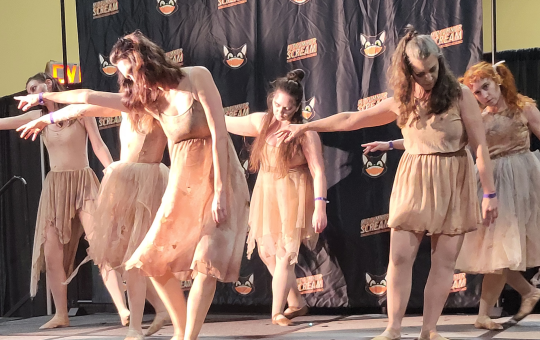 a group of dancers, dressed in bloody shabby clothes, reach to the left, heads down