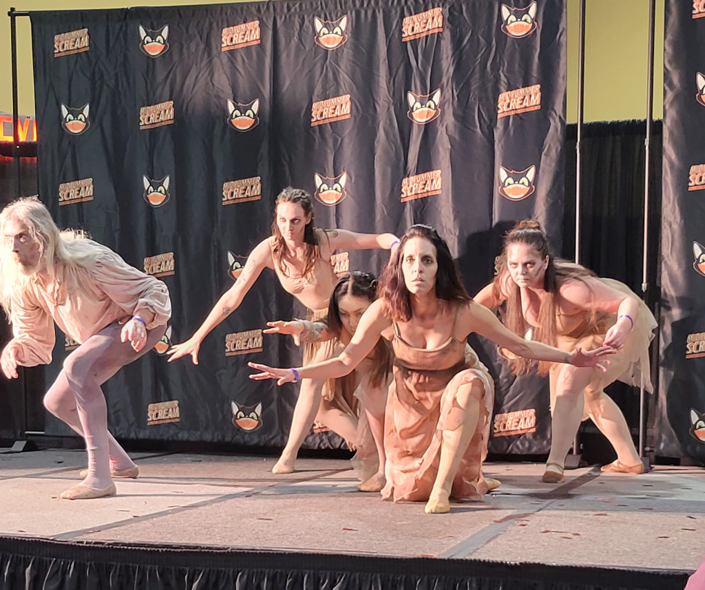 a group of dancers, dressed in bloody shabby clothes, crouch, looking at the audience