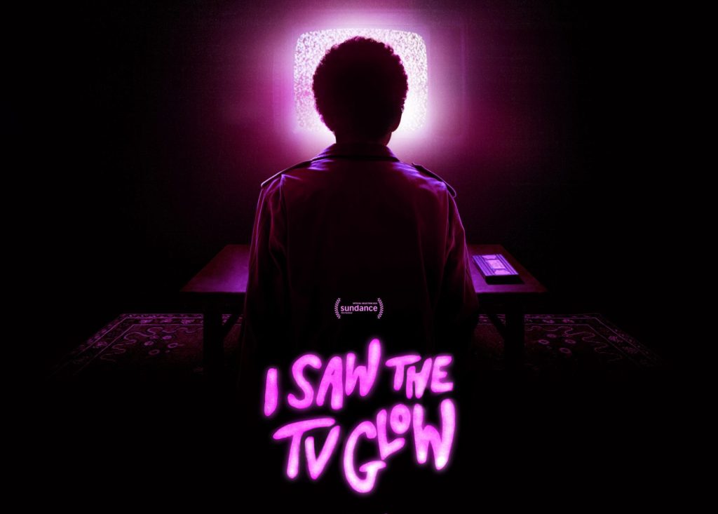 A dark image of a person sitting in front of an old television that is playing static and emitting a bright pink light. I Saw the TV Glow is writting in neon pink lettering at the bottom of the image. 