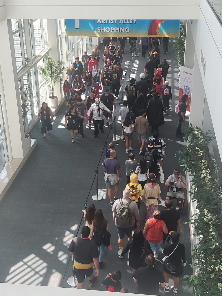 A hallway with people. A group of people on the left walking toward the camera, while a group of people on the right walk away.