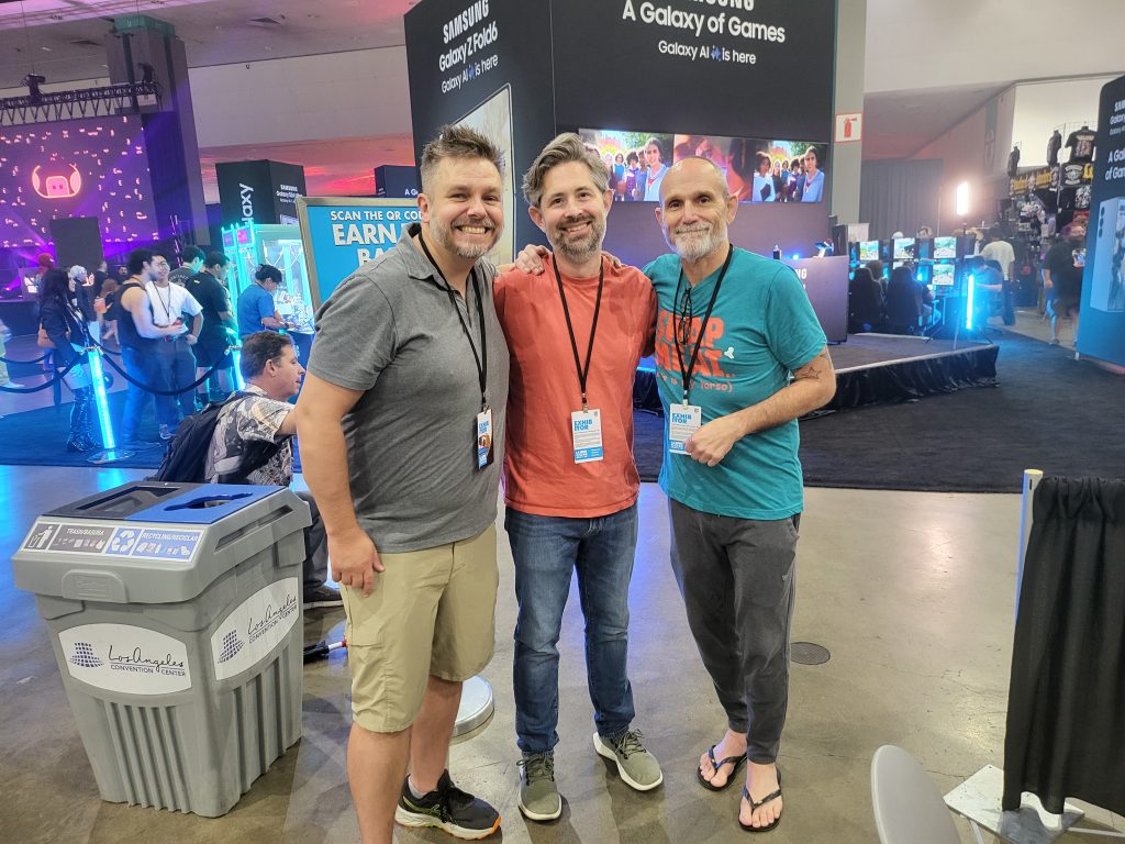 three white men stand in the middle of a booth at LA Comic Con. 