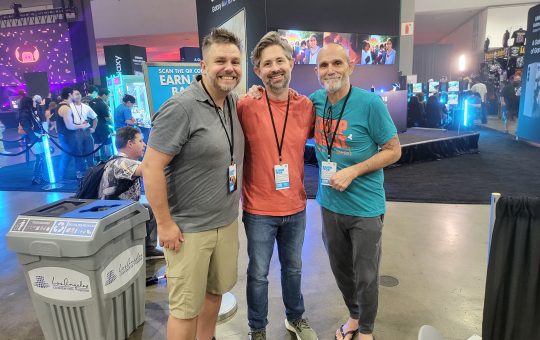 three white men stand in the middle of a booth at LA Comic Con.