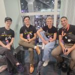 four people - two women and two men - sit on chairs facing the camera