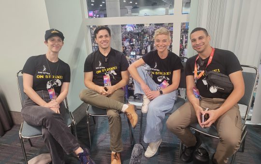 four people - two women and two men - sit on chairs facing the camera