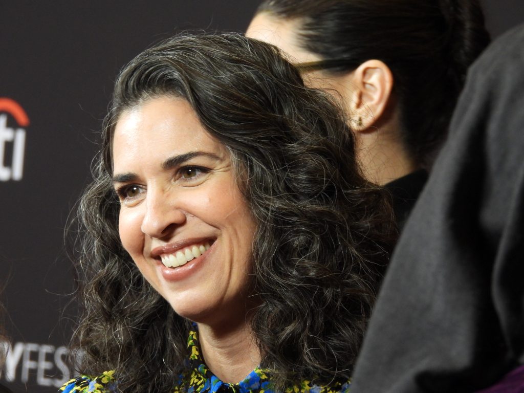 a close up of a white woman with dark hair, wearing a dress that is green and yellow, smiling