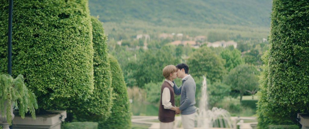 A faraway shot of Khanin and Charan kissing in a garden.