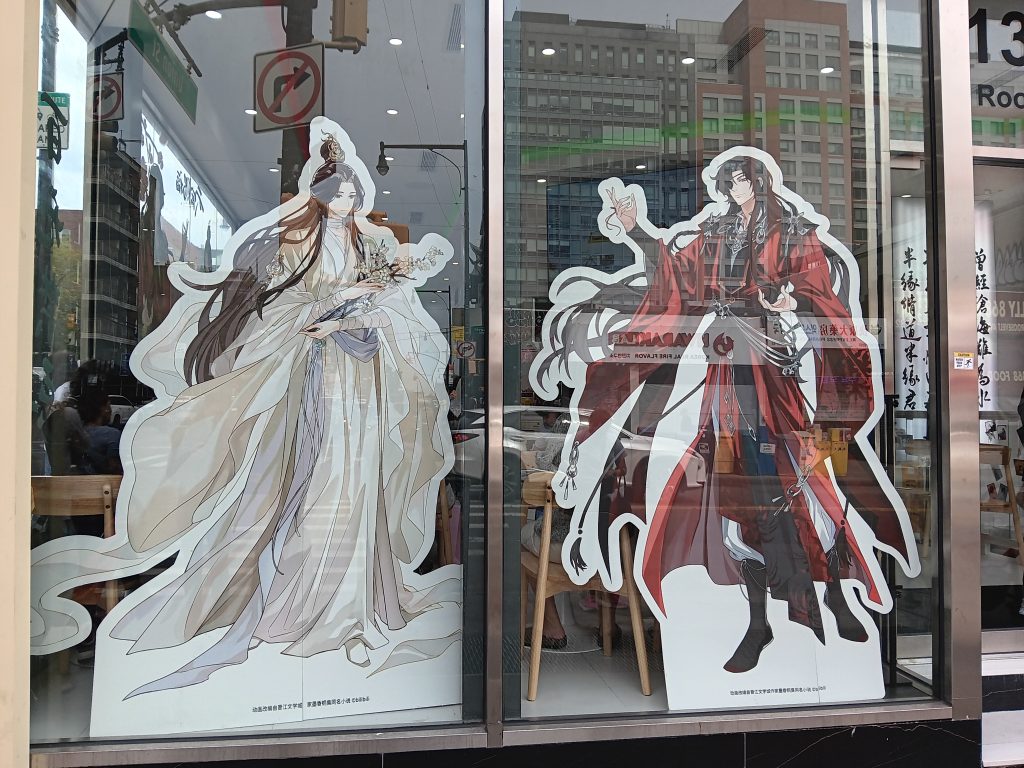 Cardboard standees of Xie Lian and Hua Cheng in the front windows of Dimension Poptown