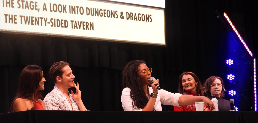 a group of five people sitting behind a table at a con; three women, one man, and one nonbinary.