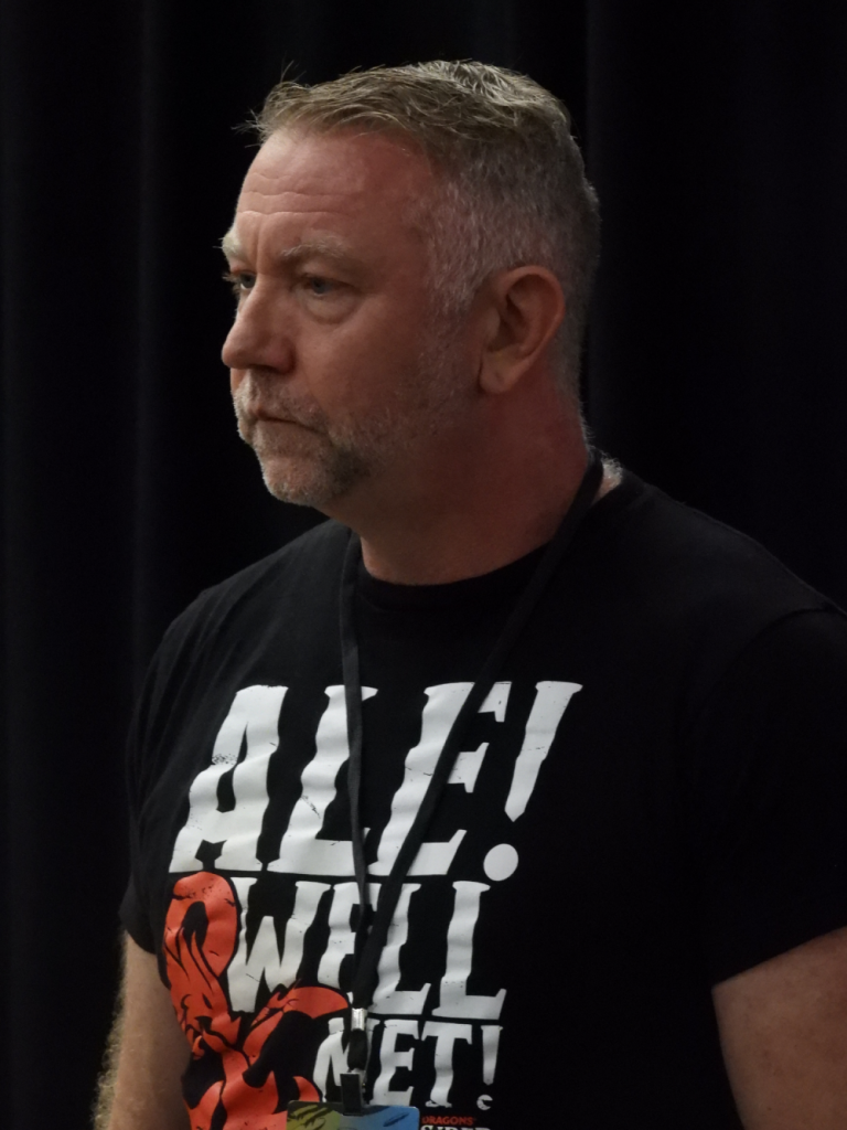 a white man with short blondish hair and a scruff wearing a black t-shirt