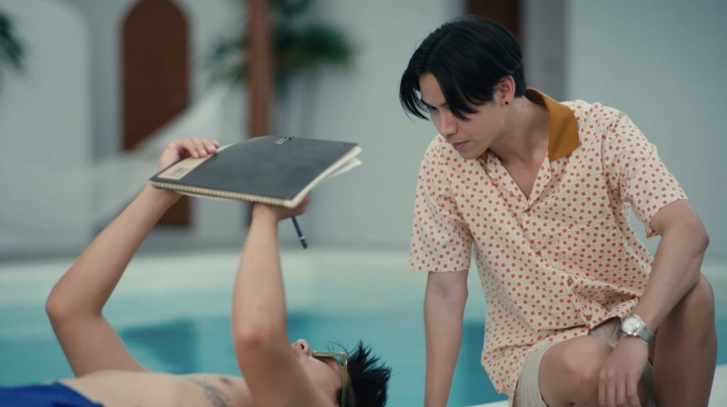 Lava lays on his back by the side of the pool. He is holding a sketchbook above him and is drawing something. Wave sits beside him, leaning forward so that he is hovering over Lava's face.