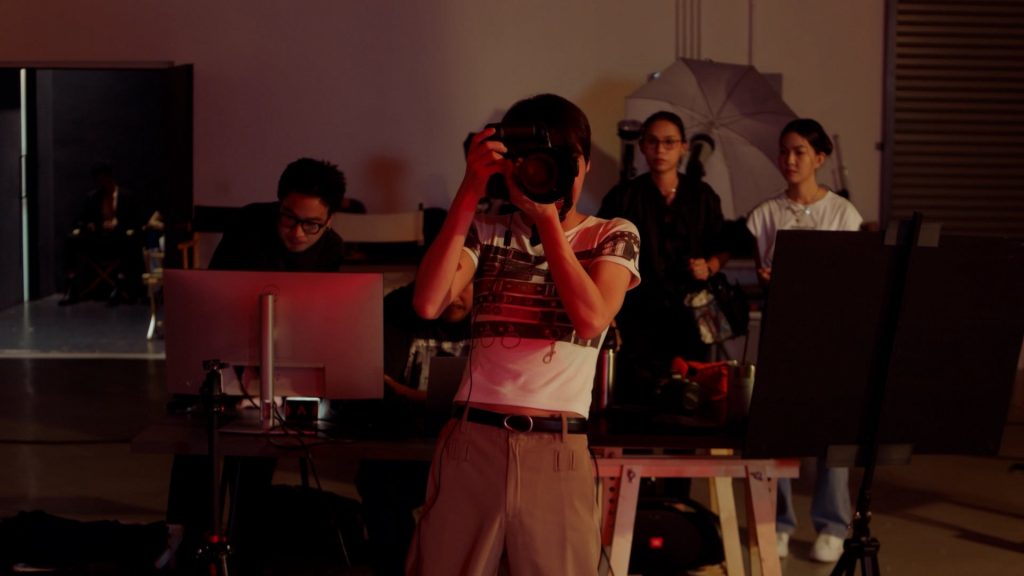 Jira takes photos at a photo shoot. He leans slightly back, with the camera raised to shoot.