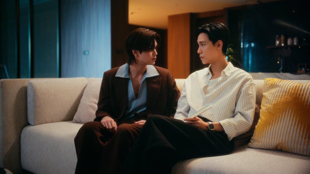 Pai and Tim sit close together on the sofa, angled toward each other. Tim is holding an architect's triangular scale.