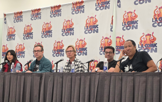 five people sitting at a table, the LA Comic Con logo on banners behind them