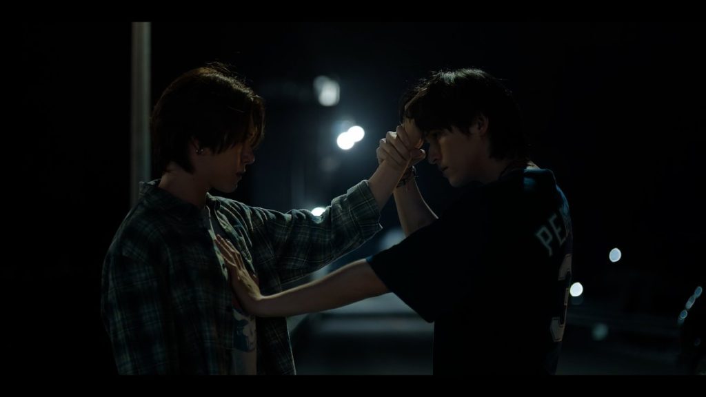 On a dark street, Niran places his hand on Pete's chest, and hold's Pete's hand to his own forehead.