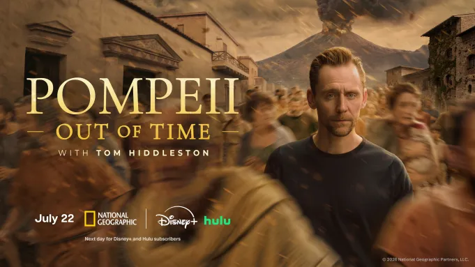 Tom Hiddleston stands amid a blurry group of people, the Romans of Pompeii.
