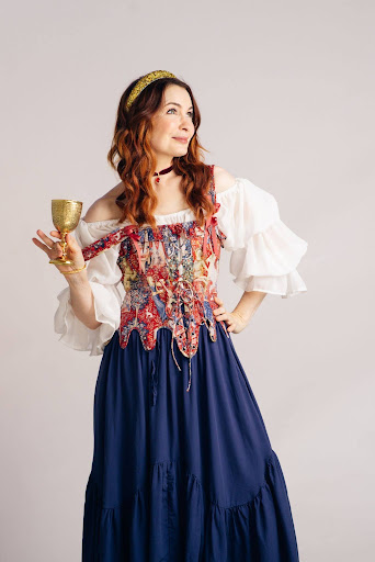 A white woman with long red hair wearing a Renaissance Festival dress